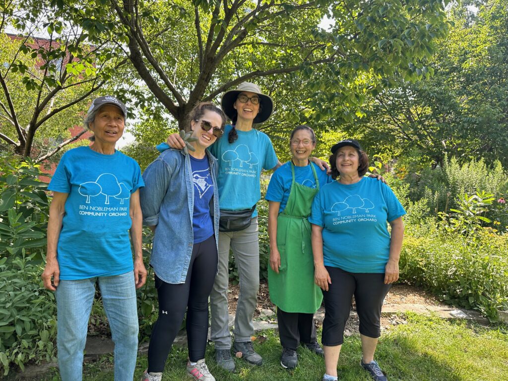 Women in front of ornamental cherry trees wearing Ben Nobleman Park Community Orchard T shirts