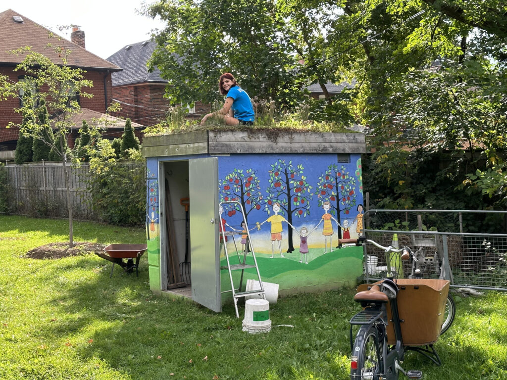 Girl sitting on top of green roof on shed in Ben Nobleman Park Community Orchard