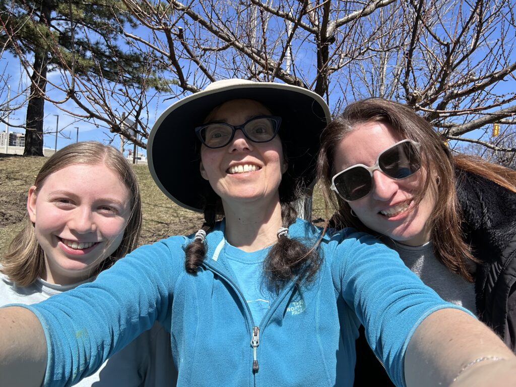 Selfie of Eleanor, Susan and Carolyn looking at the camera with apricot trees in background.